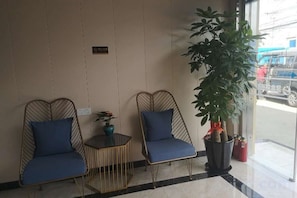 Dos sillas azules con estructura metálica, una mesa pequeña con un florero y una planta, y una planta grande en maceta cerca de una ventana.