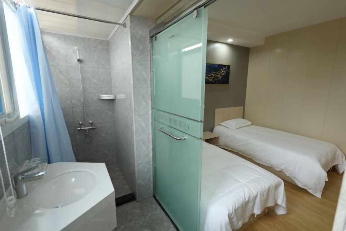 A hotel room with a bathroom, a shower, a sink, and two beds.