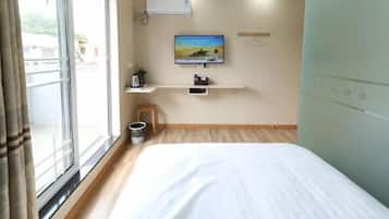 Quarto de hotel com cama, televisão fixada na parede, mesinha e janela com cortinas.