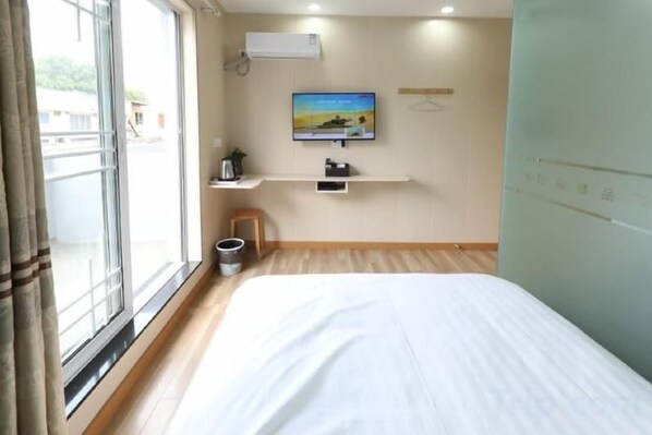 Habitación de hotel con una cama, televisión montada en la pared, una mesita pequeña y un ventanal con cortinas.