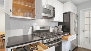 Una cocina con armarios blancos, una estufa de acero inoxidable, un microondas y un refrigerador.