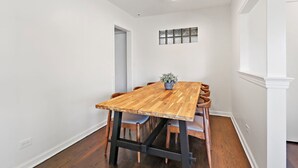 Un comedor con mesa y sillas de madera, un jarrón con flores y una ventana con detalles decorativos.