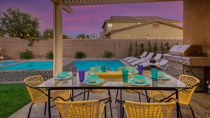 Eine Außenpatio mit Pool, Liegestühlen, einem Grill und einem Esstisch.