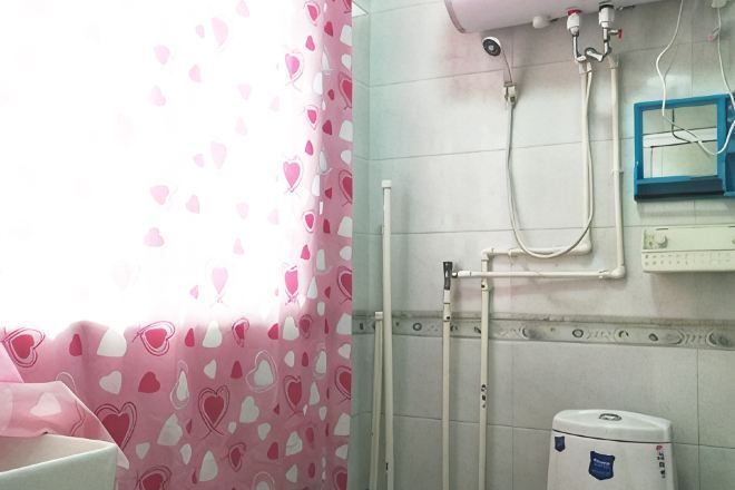 Casa de banho com chuveiro, sanita e janela com cortinas estampadas em formato de coração.