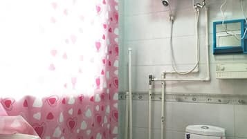 Casa de banho com chuveiro, sanita e janela com cortinas estampadas em formato de coração.
