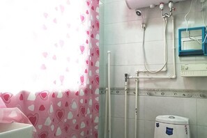 Un baño con ducha, inodoro y una ventana con cortinas de estampado de corazones.