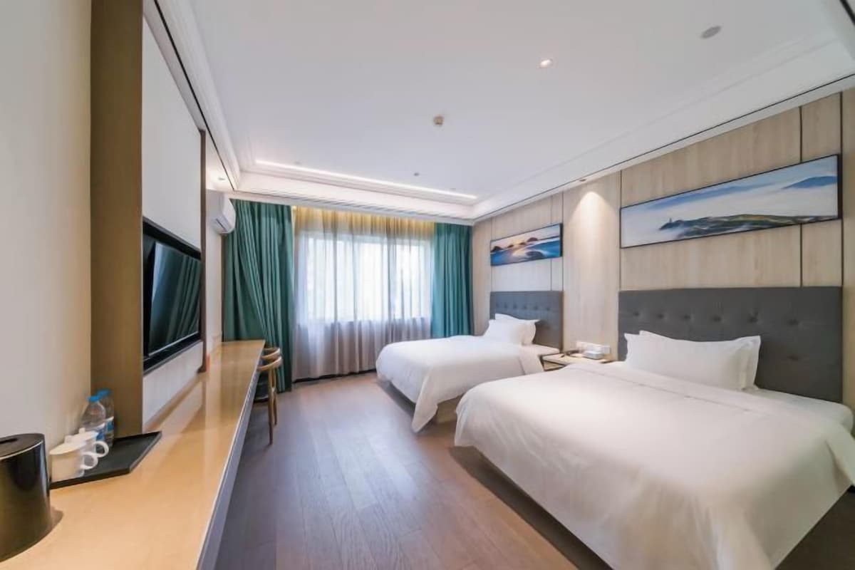 A hotel room with two beds, a TV, a desk, and a window with curtains.