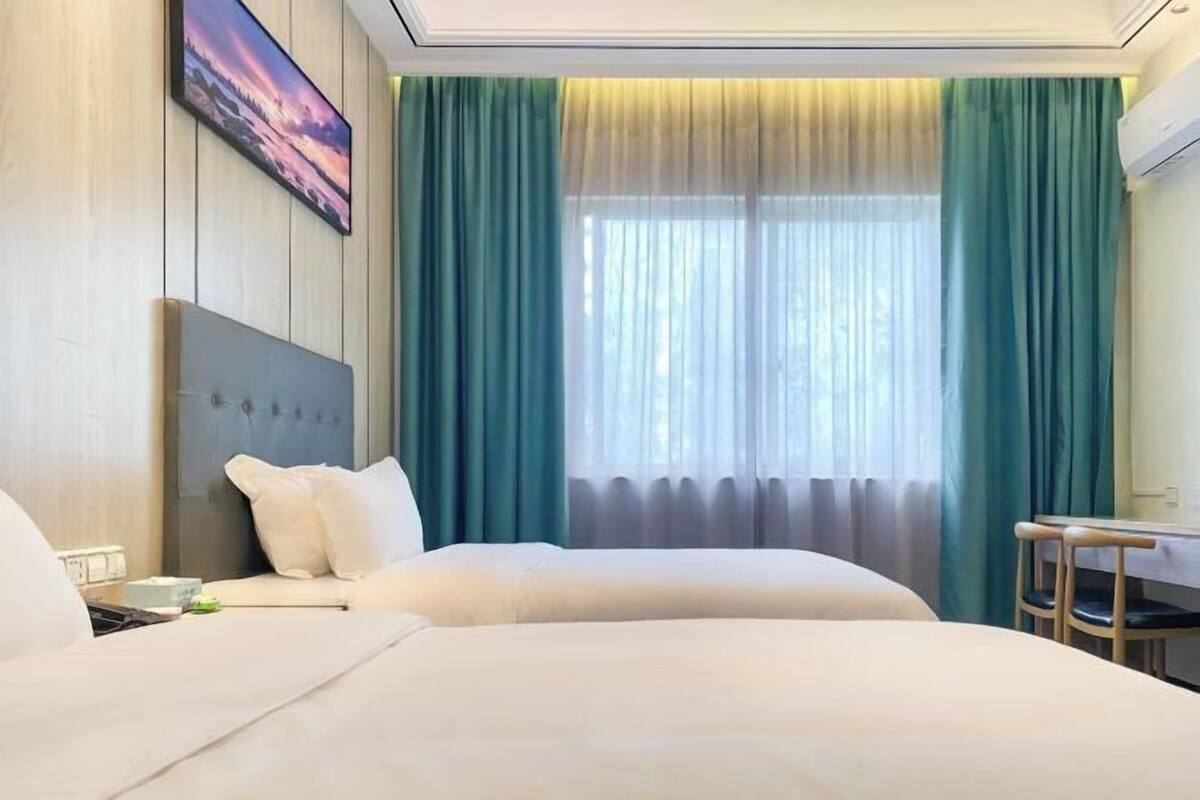A hotel room with two beds, a desk, a chair, and a large window with curtains.