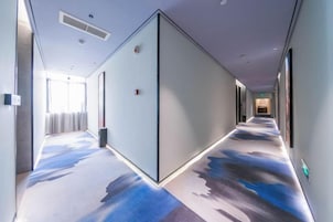 Un pasillo de hotel con alfombra estampada, separadores de vidrio y vistas al vestíbulo.