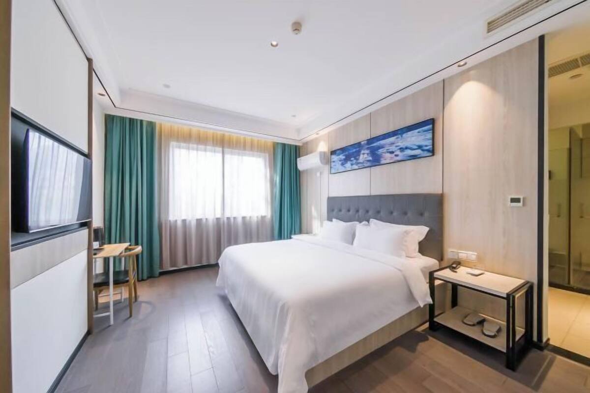 A modern hotel room with a large bed, a desk, a chair, a TV, and a painting on the wall.