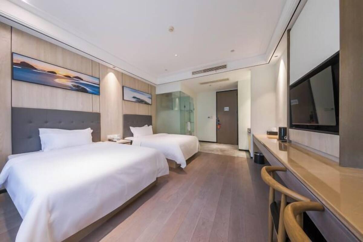 A hotel room with two beds, a TV, a desk, and a painting on the wall.