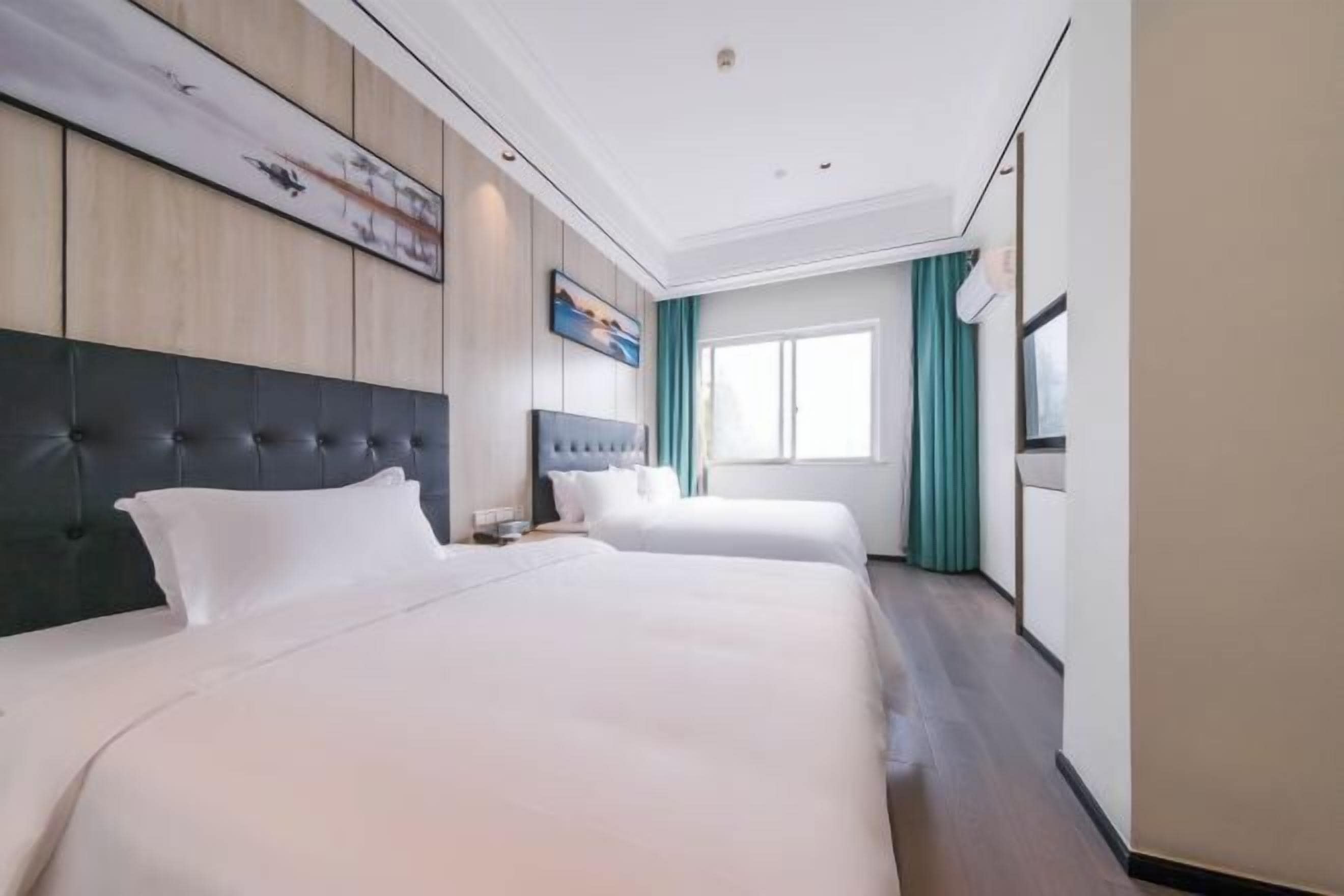Une chambre d’hôtel avec deux lits, une grande fenêtre et un tableau au mur.