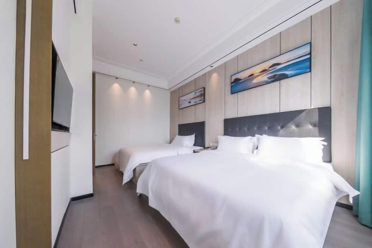 A hotel room with two beds, a flat-screen TV, wooden panel walls, and artwork.