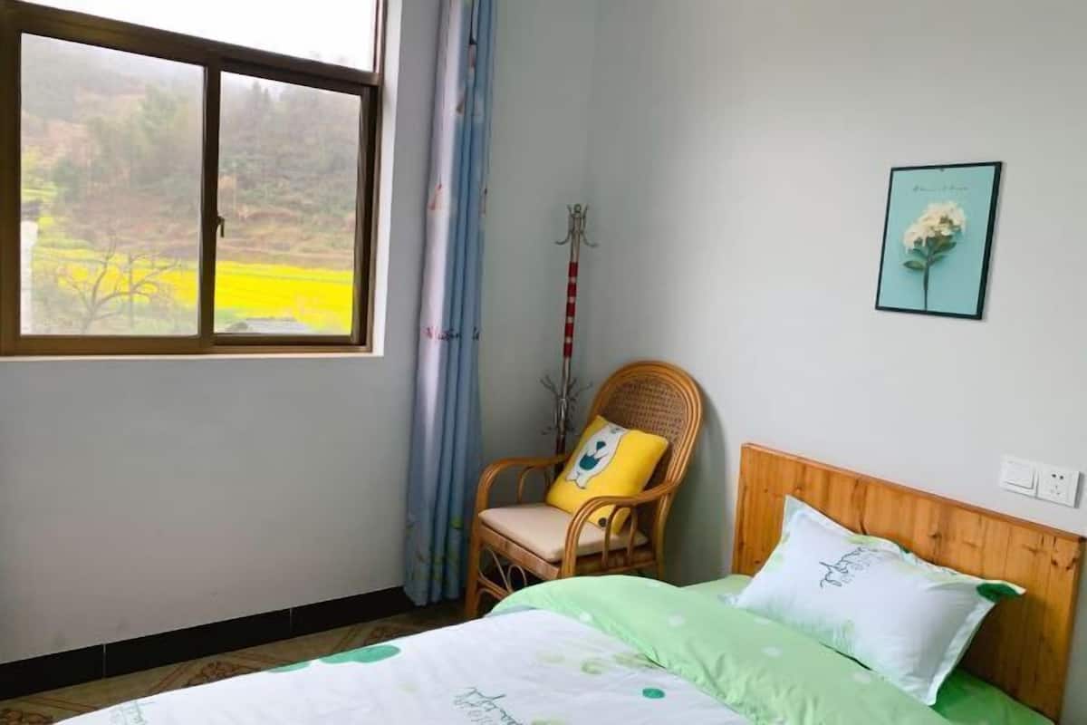 A bedroom with a bed, a chair, a window, and a wall-mounted picture.