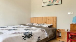 Une chambre à coucher avec une tête de lit en bois, un lit recouvert d’une couvre-lit à motifs de feuilles, une table de chevet avec une lampe et un fauteuil rouge.