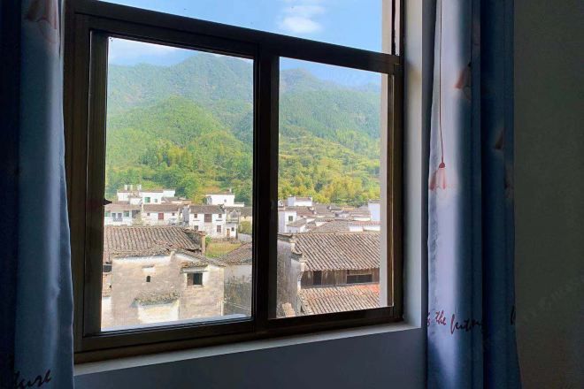 A window with a view of traditional buildings and green hills.