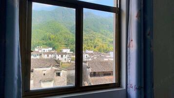 A window with a view of traditional buildings and green hills.