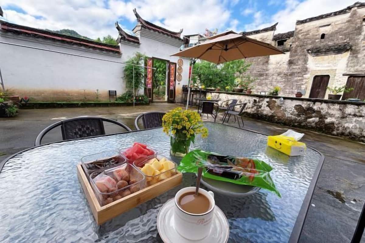 A table with a cup of coffee, a tray of snacks, and a vase of flowers in an outdoor setting with traditional architecture.