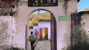 Une porte d’entrée de style chinois traditionnel mène à un bâtiment sur lequel une enseigne indique qu’il s’agit d’un restaurant et d’un lieu d’hébergement.