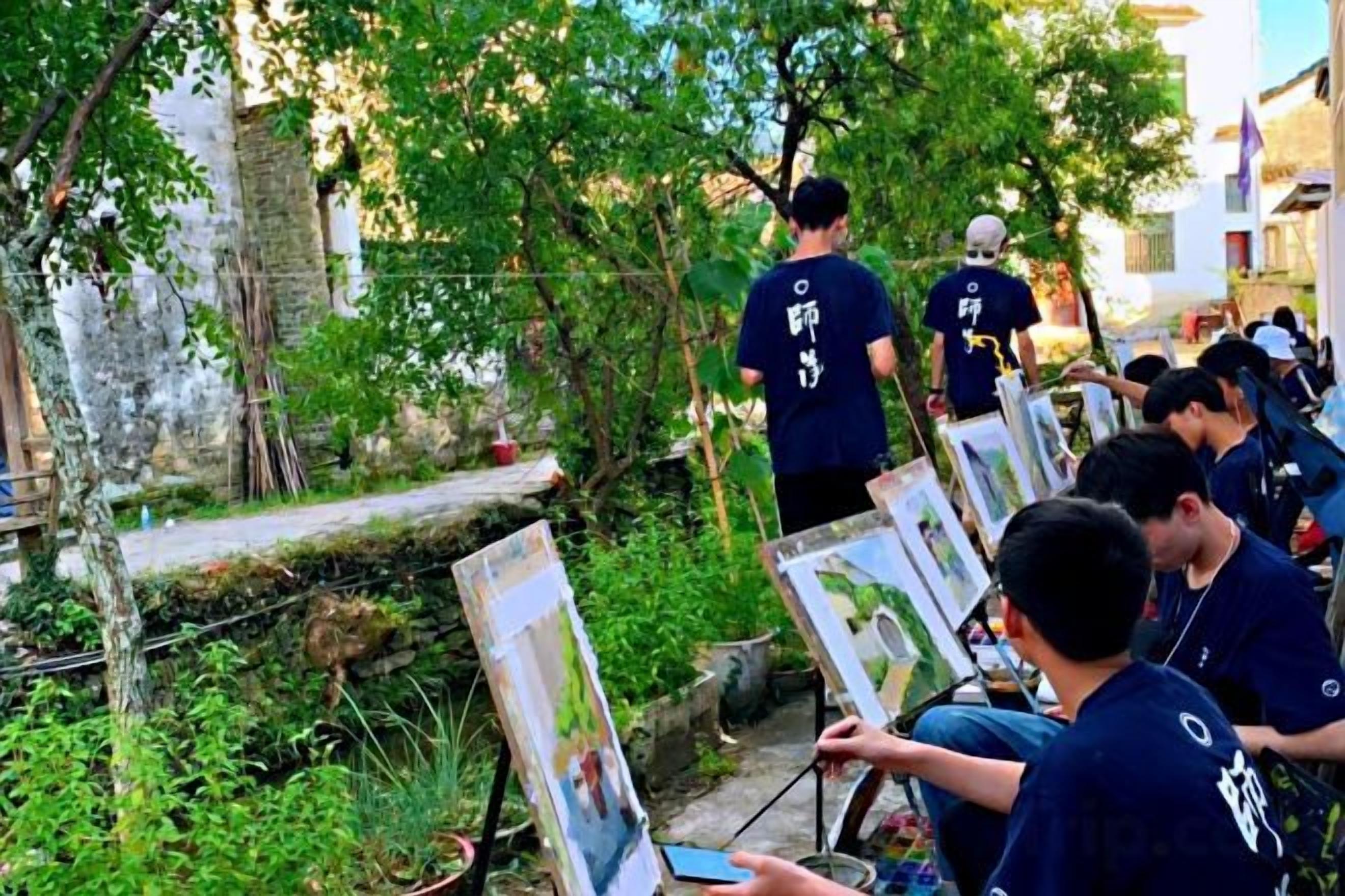 A group of people outdoors, some holding up paintings, possibly at an art event or exhibition.