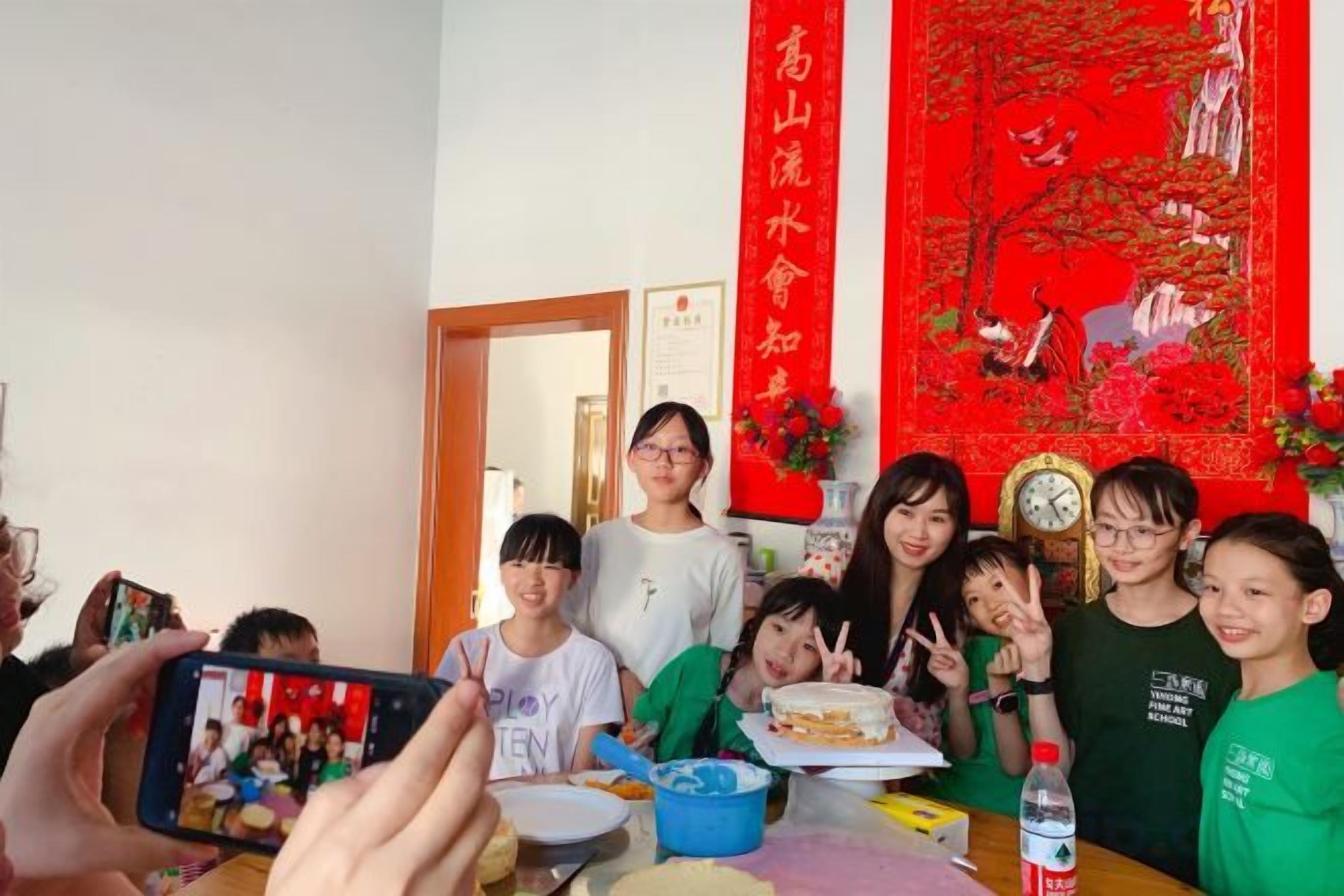 Un grupo de personas sentadas alrededor de una mesa con comida y bebidas, un reloj y un tapiz decorativo rojo.
