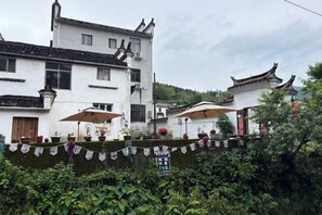 A traditional building with a white facade, multiple windows, and a balcony with umbrellas. - Xiaotaoyuan Inn (Wuyuan)