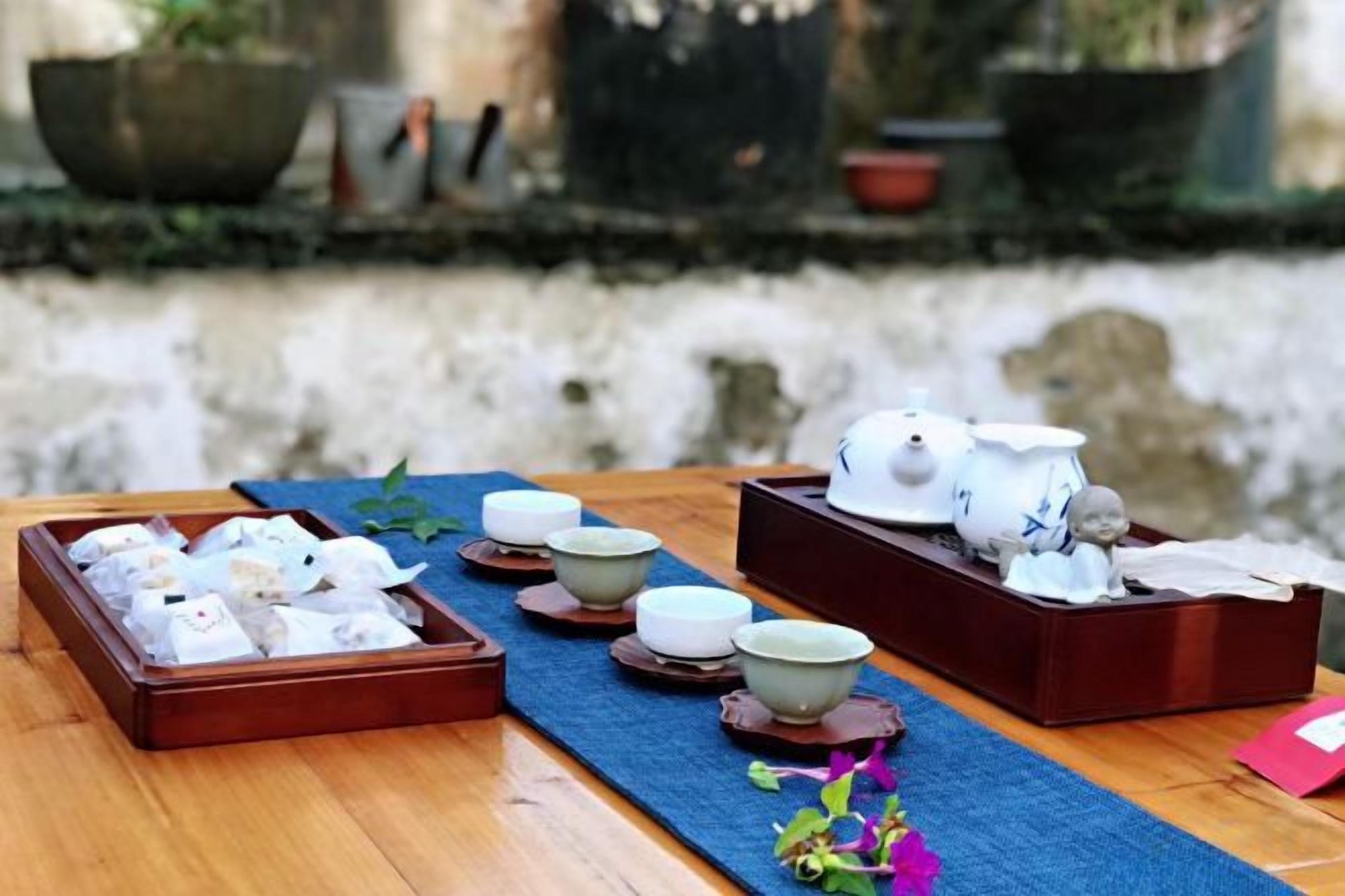 A table with tea sets and teapots, arranged on a wooden table with a blue mat.