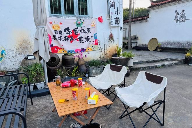 An outdoor seating area with a table and chairs, potted plants, and a decorative banner.