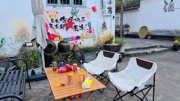 An outdoor seating area with a table and chairs, potted plants, and a decorative banner.