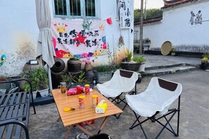 An outdoor seating area with a table and chairs, potted plants, and a decorative banner. - Xiaotaoyuan Inn (Wuyuan)