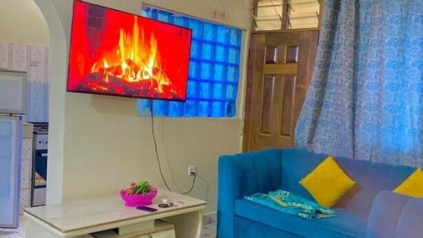 A living room with a blue sofa, a television mounted on the wall, and a small table with a pink bowl and a plant. - Bondeni Mombasa city (Mombasa)