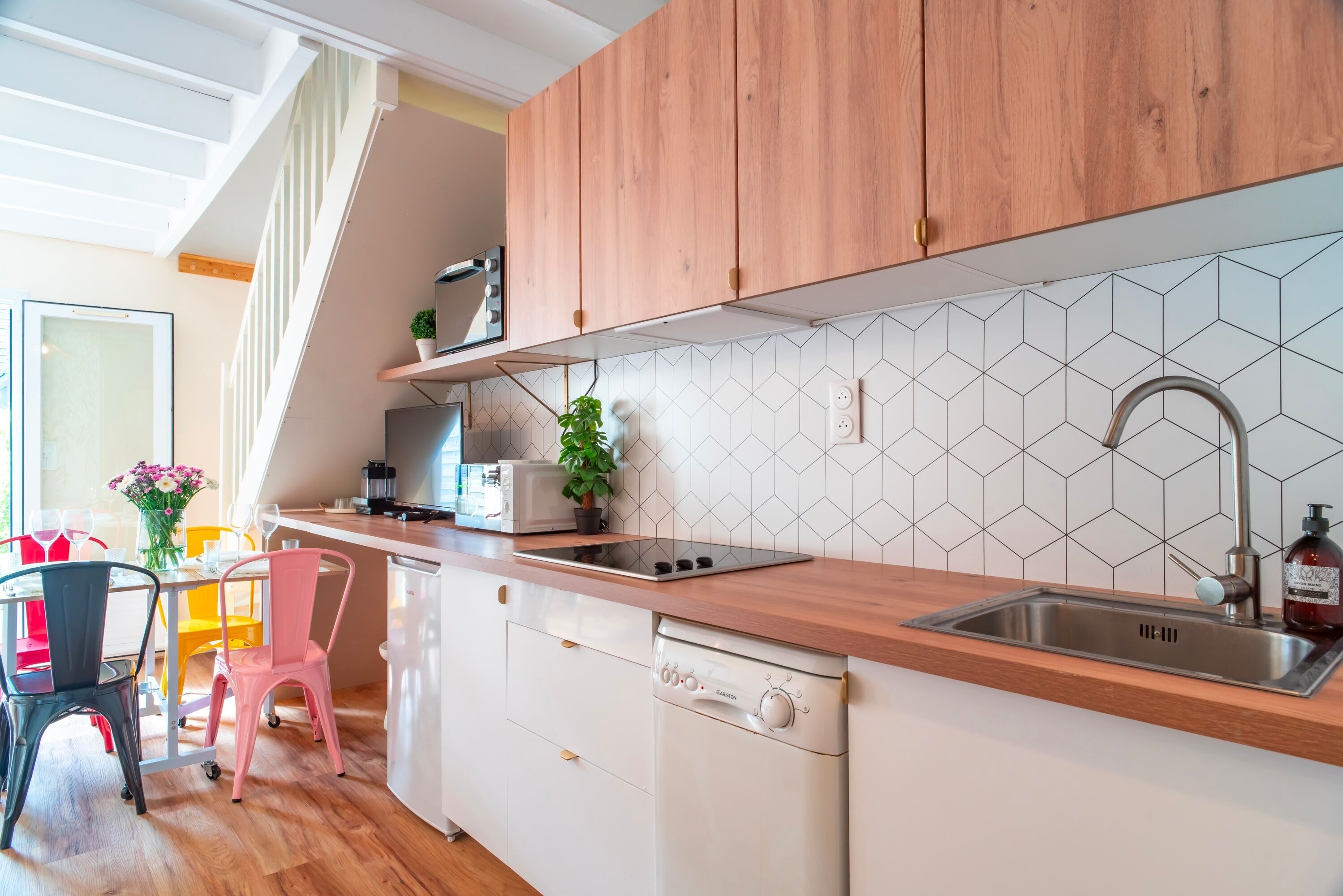 Een moderne keuken met houten kastjes, een roestvrijstalen spoelbak en een vaatwasser. Boven de spoelbak bevindt zich een raam en op het aanrecht staat een plant.