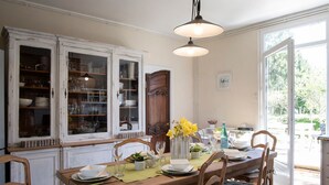 Un comedor con una mesa de madera dispuesta para cuatro personas, rodeada de sillas. Un aparador grande con puertas de vidrio está a la izquierda, y una puerta a la derecha da al exterior.