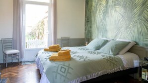 Un dormitorio con una cama, dos sillas, una ventana y una pared con un diseño de hojas de palma.