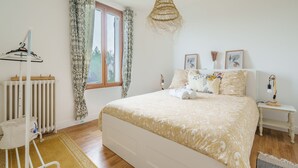 Une chambre avec un grand lit, un radiateur, une fenêtre avec des rideaux, un luminaire suspendu et une table de chevet avec une lampe.