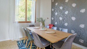 Un coin repas avec une table en bois, des chaises grises, un vase avec des plantes et un mur orné de motifs.