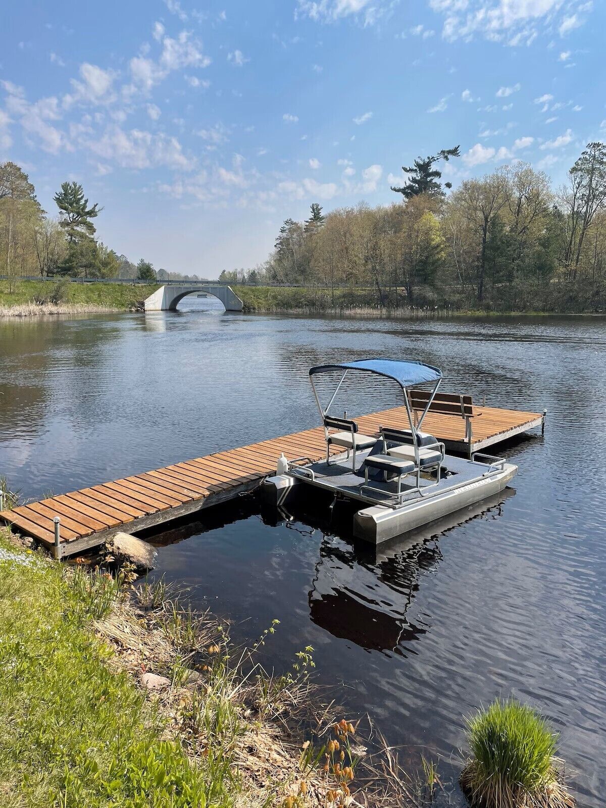 A calm river with a wooden dock and a small boat docked at the end.