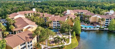 A resort with multiple buildings, a central pool, and a lake.