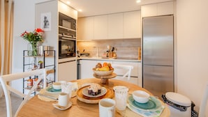 Una cocina moderna con una mesa de desayuno dispuesta, con un frutero, pasteles y tazas de café.