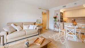 Una sala de estar moderna con un sofá color beige, una mesa de centro de madera y un comedor con sillas blancas y una mesa de madera.