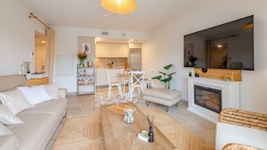 Una sala moderna con sofá, mesa de centro y chimenea. Se ve un comedor con sillas y una cocina al fondo.