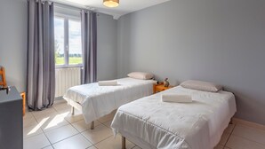 Ein Zimmer mit zwei Betten, einem Fenster mit Vorhängen, einem kleinen Tisch und einer Lampe.