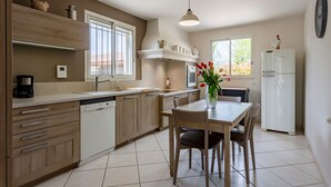 Eine moderne Küche mit Holzausstattung, einem Geschirrspüler, einem Esstisch mit Stühlen, einem weißen Kühlschrank und einer Vase mit Blumen.