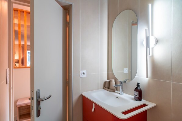 A bathroom with a white sink, red cabinet, and a large mirror.