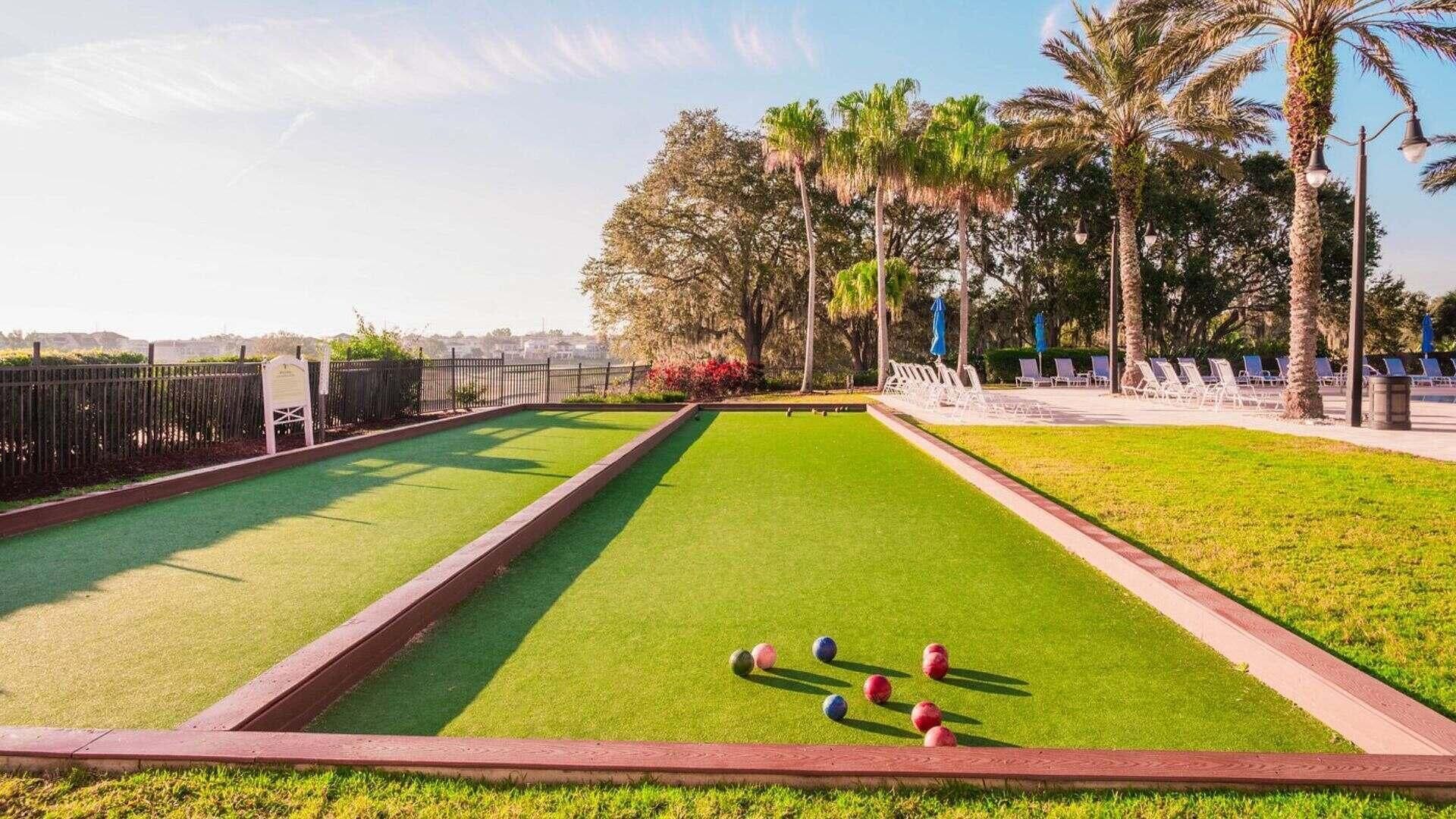 Un campo de croquet con cerca de madera, palmeras y sillas de descanso.