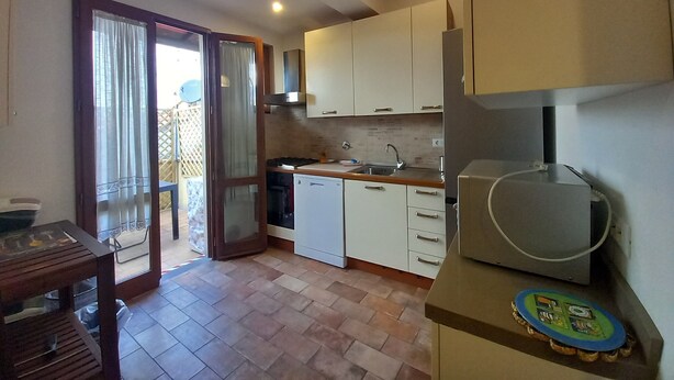 Eine kompakte Küche mit einer Schiebetür zum Balkon, einem kleinen Esstisch und einem Kühlschrank.
