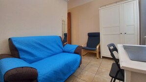 Ein Zimmer mit einem blauen Sofa, einem Sessel, einem kleinen Tisch und einem Kleiderschrank.