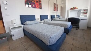 Ein Hotelzimmer mit zwei Betten, einem Schreibtisch, einem Stuhl, einem Spiegel und einem farbenfrohen, abstrakten Gemälde an der Wand.