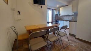 Eine kompakte Küche mit Essbereich, inklusive Tisch und Stühlen, sowie einem an der Wand montierten Fernseher.