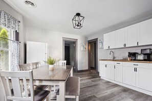 Una cocina moderna con armarios blancos, una mesa de comedor de madera y una lámpara colgante negra.